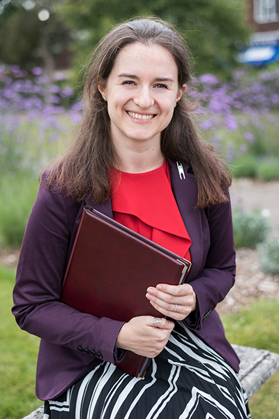 Steph Kendrick sitting in a blossoming garden, holding a red ceremony book